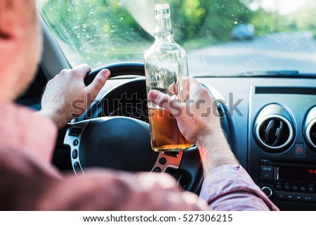 In the picture a man drinking alcohol in the car.