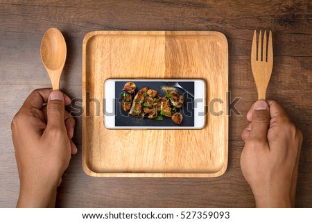 Food photo in smartphone with two hand holding a spoon and fork. The food and social media concept