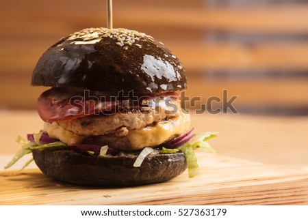 Concept: restaurant menus, healthy eating, homemade, gourmands, gluttony. Trendy glossy burger with beef in black bun with ingredients on messy vintage wooden background.