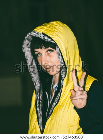 A young girl in a yellow jacket shows thumbs up sign of victory. Focus on hand, shallow depth of field, toning photo