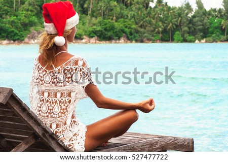 young woman in christmas hat meditating in a yoga pose at the beach