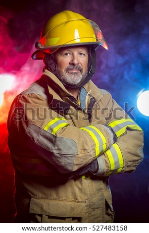 Portrait of a fireman wearing Fire Fighter turnouts and helmet.  Background is red and blue smoke and light.  Turnouts are protective clothing.