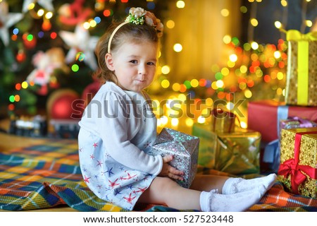 beautiful little girl, sits on a floor with a gift in hands, in a festive interior. A set of bright sparks on a background