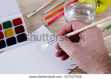 The artistÃ¢??s hand drawing a paint, brushes and pencils. Art background