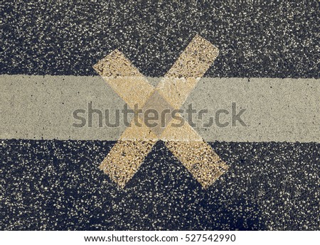 Vintage looking White line with yellow cross sign on black tarmac asphalt
