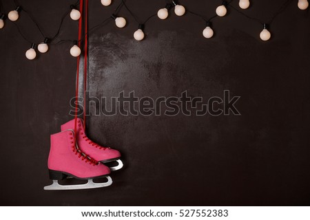 Christmas decoration with vintage skates on dark wooden wall with twinkling garland. Side view, copy space.