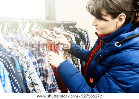 young brunette woman in a blue jacket chooses clothes in a store. Woman buys clothes.