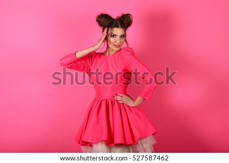 Beautiful and stylish brunette girl in the image of a doll posing on a background of a pink wall
