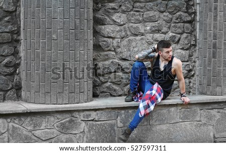 Young tattooed man posing on stone wall background