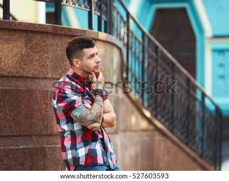 Young tattooed man posing on blurred building background