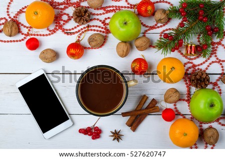 Christmas decorations and smart phone on a wooden table. New year decoration on a wooden table: tree branch, tangerines and walnuts.