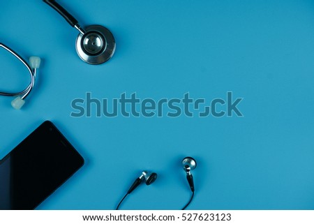 Flat lay of stethoscope, earphone and smartphone on navy blue background.