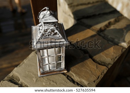 Wooden lantern with white candle inside stands on stone wall