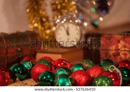 Christmas holiday red, green, yellow and silver decoration hanging and on the table with a treasure box and present box and a clock in the background showing 5 minutes to twelve.