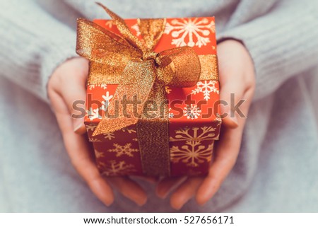 Woman's hands holding christmas or new year decorated red gift box with gold ribbon. Toned picture