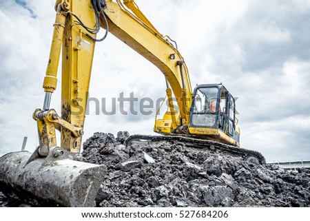 Yellow excavator is making pile of soil by pulling ground up on heap at construction site, project in progress. Royalty-Free Stock Photo #527684206