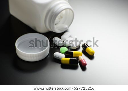 Capsules spilled from pill bottle on dark background with reflection
