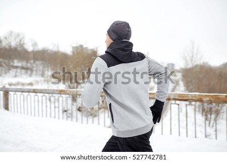 fitness, sport, people, season and healthy lifestyle concept - young man running along snow covered winter bridge road (motion blurred picture)