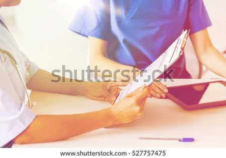 hospital, profession, people and medicine concept - close up of doctors with tablet pc computer and clipboard reading medical report at medical office