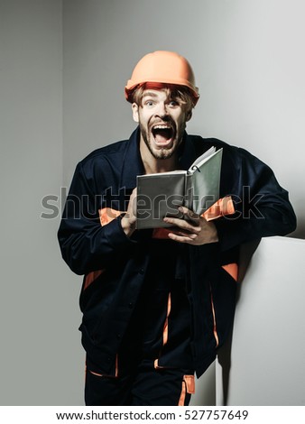 Excited man shouting handsome builder repairman craftsman foreman or construction worker in orange hard hat and boilersuit keeps accounting book on grey background