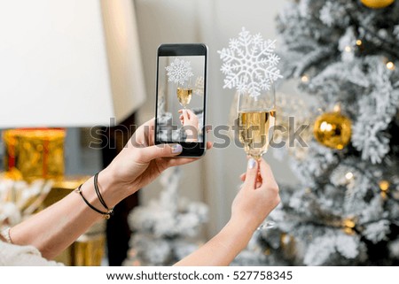 Photographing with smart phone a glass of sparkling wine with snow flake on the Christmas tree background