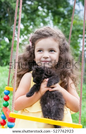 Baby girl holding a black kitten sitting on a swing outdoors