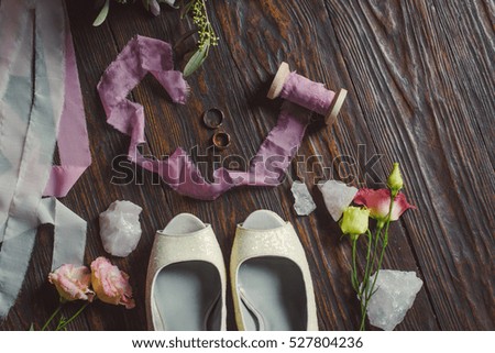 Wedding white shoes  on a wooden background near the pink ribbons, flowers and  rings.