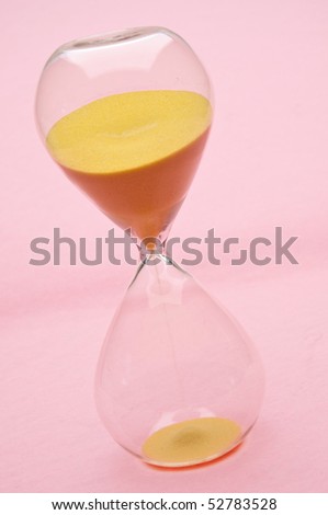 Modern Hour Glass with Yellow Sand on a Pink Background.  Time is Passing as the Sand Falls.