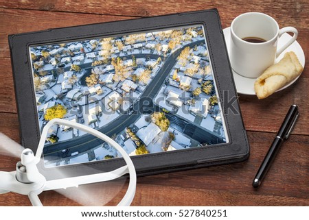 aerial photography concept - reviewing aerial pictures of city residential area in snow on a digital tablet with a drone rotor and coffee, screen picture copyright by the photographer