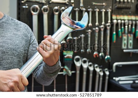 Big wrench in hands on the background wall with tool in store