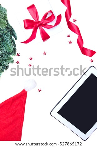 Flat lay, Top view Christmas composition isolated on white background. Digital tablet, natural green pine wreath, white gift box with red fabric tape, spiral ribbon, stars confetti. Xmas background.