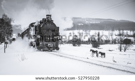 Old steam train puffing across winter landscape in Sudeten between Czech Republic and Germany. Vintage looking photo of transportation from 19th century, 20th century in Europe. Black and white.Retro