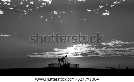 Cloudy sunset and silhouette of crude oil pump in oil field - Black and white 
