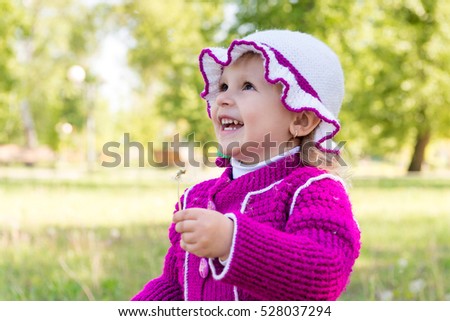 The child, a little girl blowing on a dandelion. Walk through the park in spring. Carefree childhood.