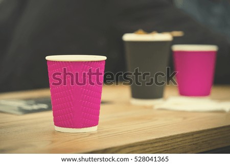 Black and pink craft paper coffee cups in cafe on wooden table, toned. Lifestyle, coffeeshop concept.