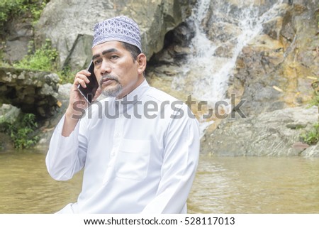 Muslim adult using smartphone at waterfall.