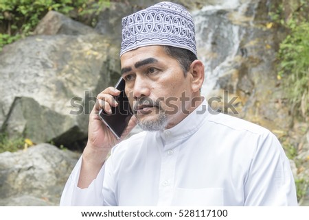 Muslim adult using smartphone at waterfall.