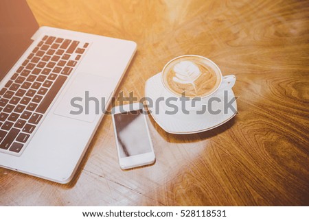 cup of latte art coffee and Laptop on wood table.