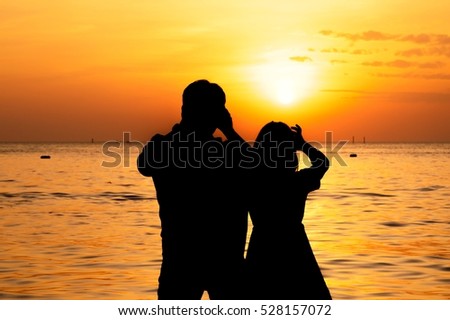 Silhouette of couple taking picture on the beach at sunset