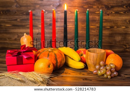 african Kwanzaa festive concept with decorative candles red, black and green, gift box, pumpkins, ears of wheat, grapes, orange, banana, bowl and fruits on wood background