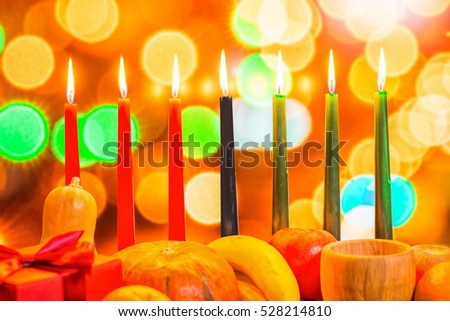 african Kwanzaa festive concept with decorate seven candles red, black and green, gift box, pumpkin, bowl and fruit on light blur bokeh background, close up