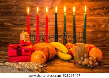 Kwanzaa holiday concept with traditional lit candles, gift box, pumpkins, ears of wheat, grapes, orange, banana, bowl and fruits on wood background