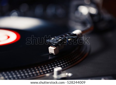 Turntables needle on vinyl record disc with music. Professional disk jokey audio equipment. Retro dj turn table records player on hip hop party in night club. Play and listen to music in high fidelity