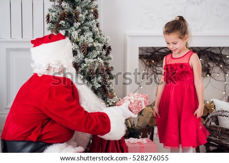 Santa Claus and children opening presents at fireplace. Kids father in costume wearing beard open Christmas gifts. Little girl helping with present sack. Family under Xmas tree over fire place on