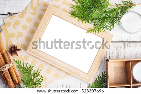Picture frame, craft paper and christmas tree brunches on white wood. Holiday mock up, handmade gift concept. Text space