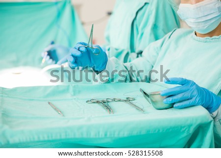 Closeup of the hands of a surgical instruments holding a pair of tweezers in an operating room