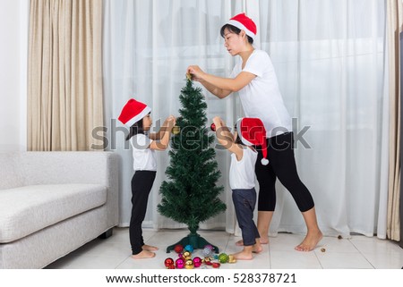 Asian Chinese mother and daughters decorating Christmas tree in the living room at home