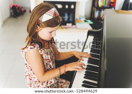 Little girl playing piano at home  Royalty-Free Stock Photo #528494629