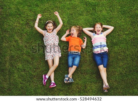 Happy children having fun outdoors. Kids playing in summer park. Little boy and two girls laying on green fresh grass Royalty-Free Stock Photo #528494632