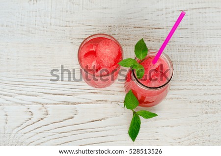 Glass of watermelon juice, mint and a jar of watermelon smoothie on a light wooden background, top view